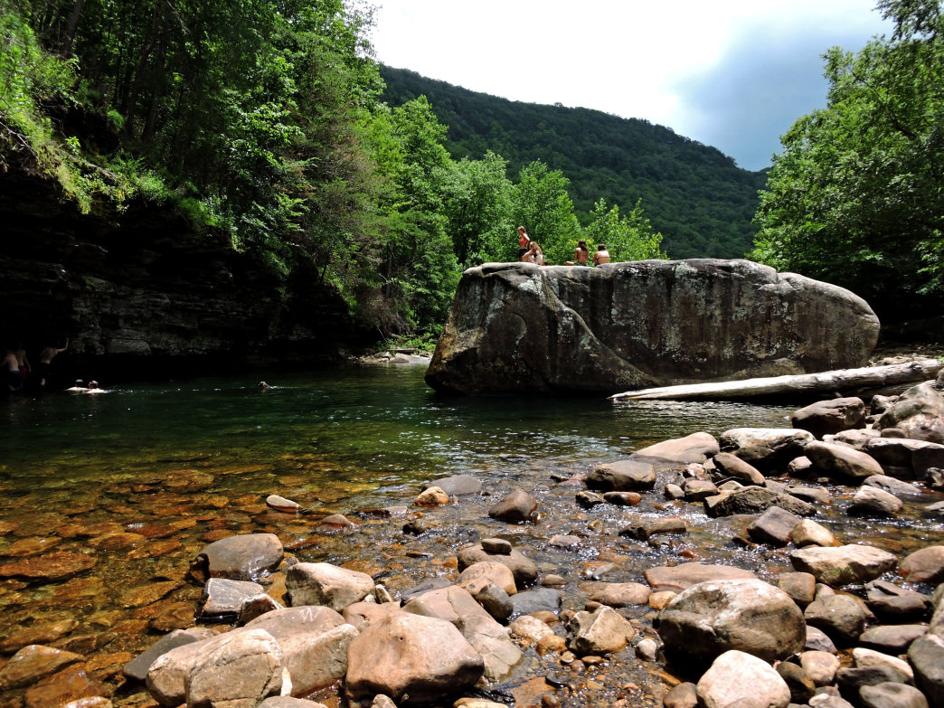 People sit atop a big rock in the middle of North Chick Blue Hole portraying the fun outdoor activity of swimming